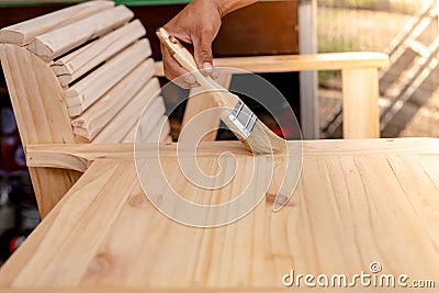 Manâ€™s hand holding a brush applying varnish paint on a wooden Stock Photo